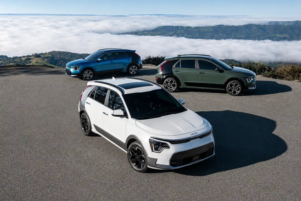 Três versões do Kia Niro híbrido estacionadas em mirante com vista para montanhas e nuvens.