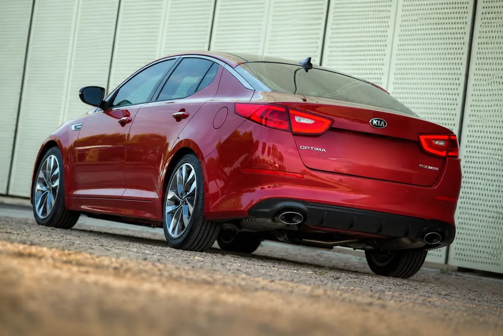 Kia Optima vermelho visto de traseira em estacionamento, sem placa traseira visível.