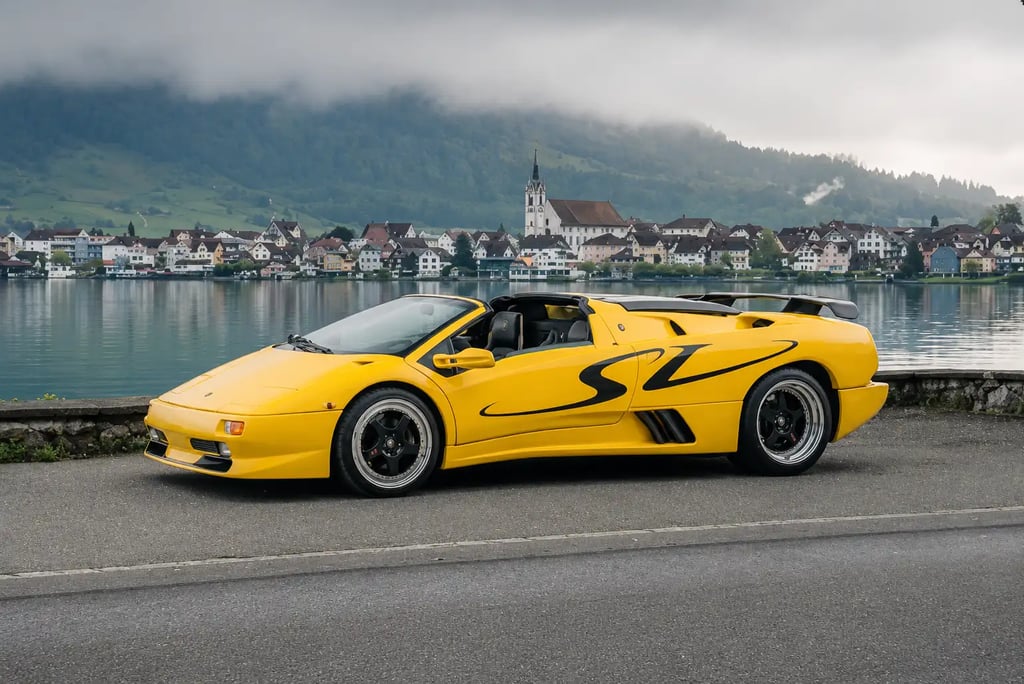 Lamborghini Diablo amarela parada à beira de lago com vila ao fundo.