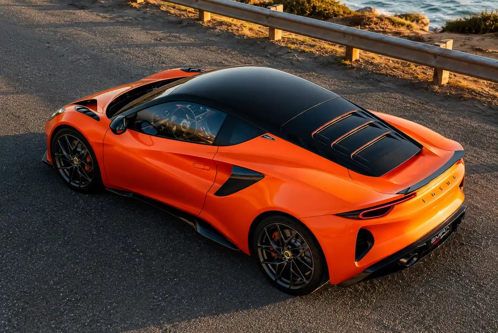 Lotus Emira 420 Sport laranja visto de cima em estrada costeira.