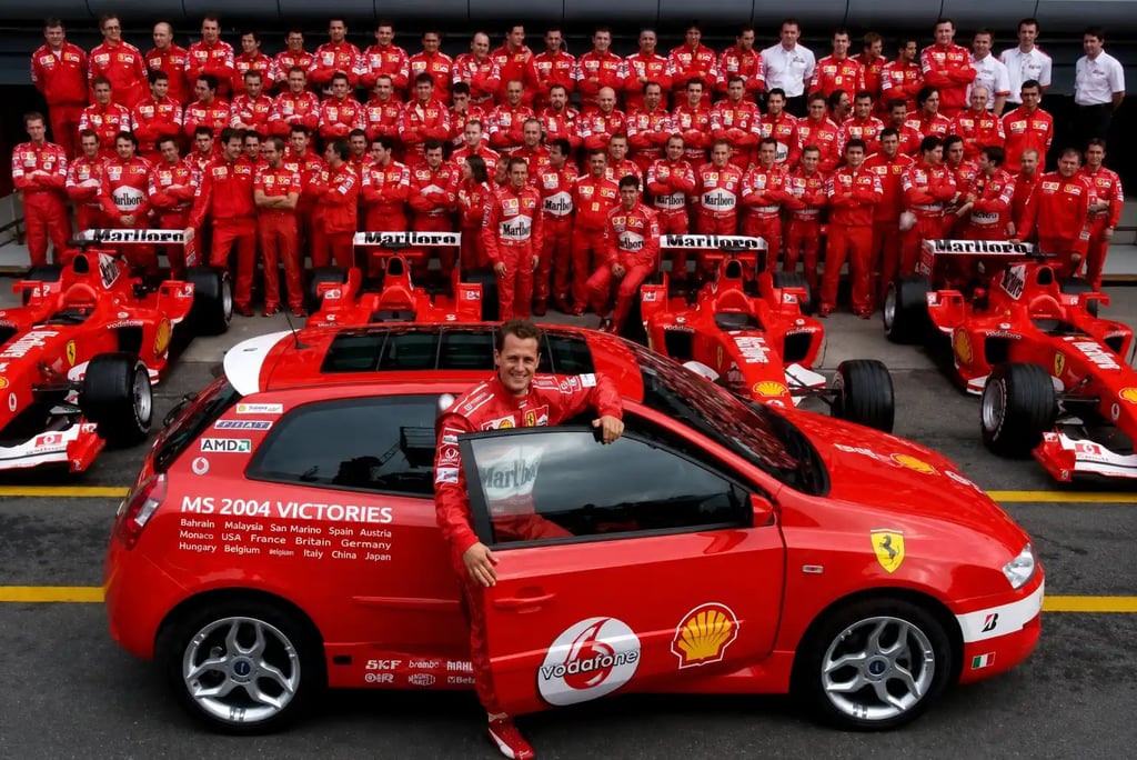 Michael Schumacher com equipe Ferrari, carros de Fórmula 1 e Stilo vermelho em 2004