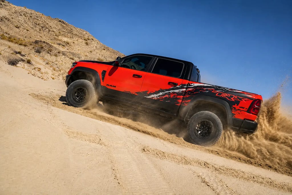 Picape Ram TRX vermelha acelerando em duna no deserto com areia levantando