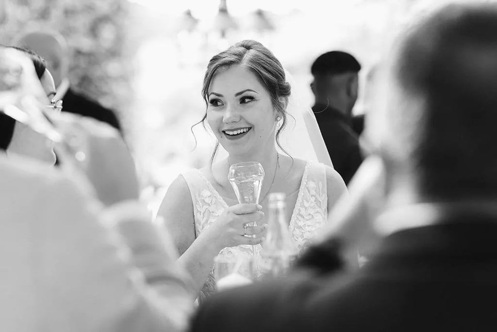 Photo en noir et blanc d'une mariée qui sourit, une coupe de champagne à la main.