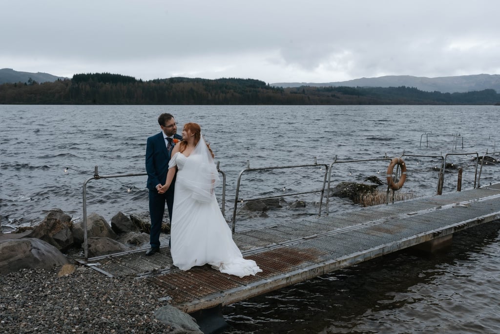 A bride and groom posing on a dock by loch venture 