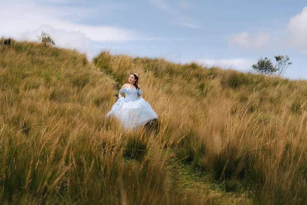 Fotografía de quinceañera con vestido celeste de princesa caminando por el prado amarillo en Quito