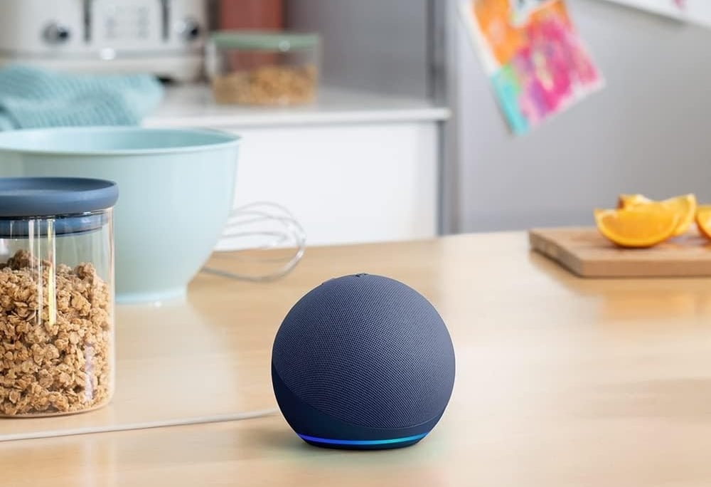 A blue Amazon Echo Dot smart speaker with a glowing light ring sits on a modern kitchen counter.
