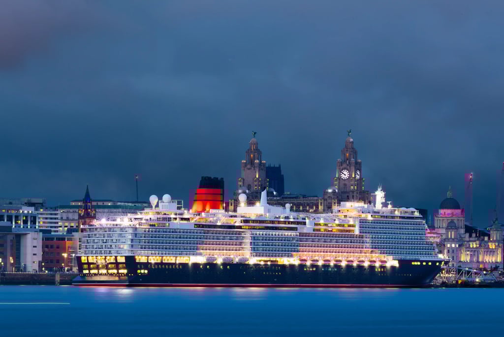 Luxury cruise ship illuminated at night at Liverpool Cruise Terminal with Liver Building in background.