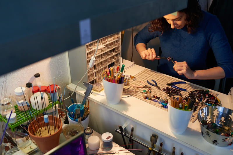 Joyero utilizando pinzas para elaborar collares artesanales con cuentas en una mesa de trabajo.