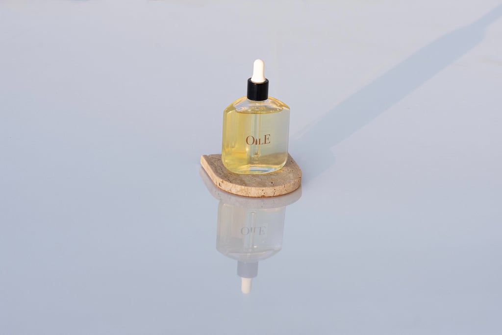 Golden facial oil serum bottle with dropper on a stone pedestal with reflective background.