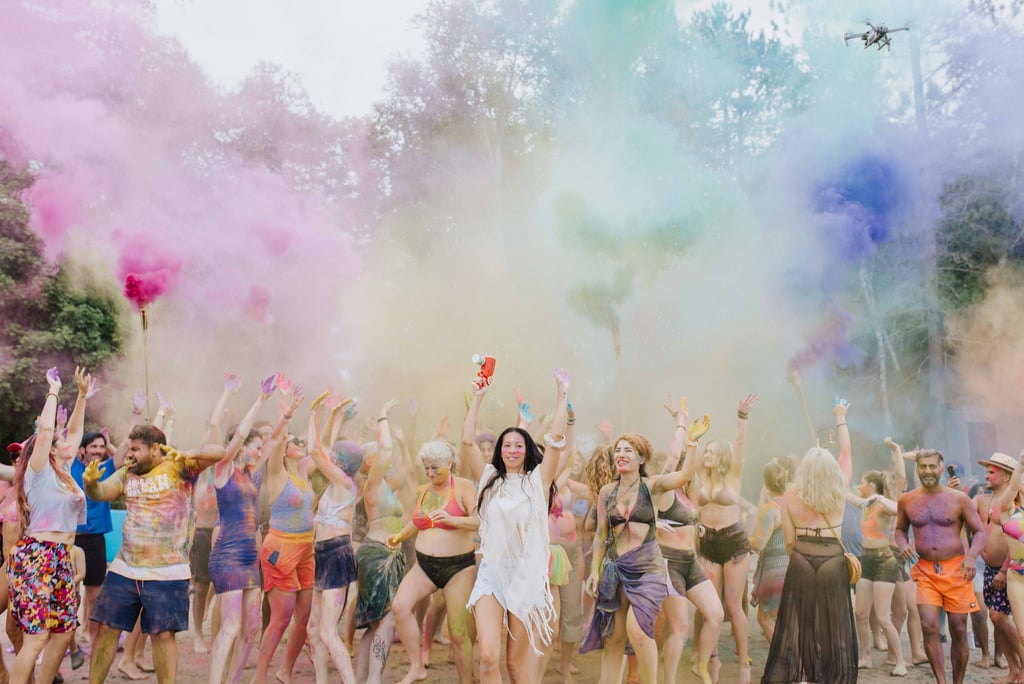 Crowd of people celebrating at a festival with vibrant clouds of purple and yellow powder.