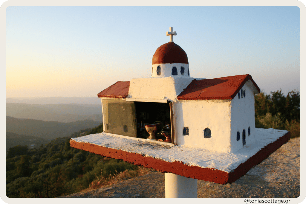 A roadside shrine with a red roof in Crete, illuminated by the sunset glow
