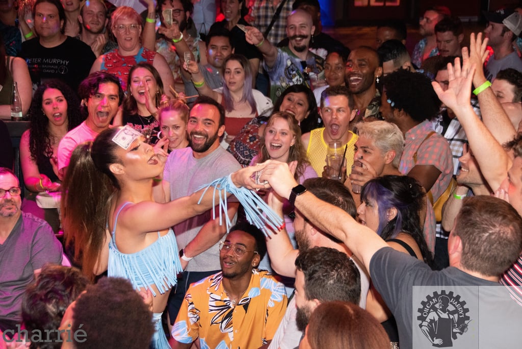 drag performer with dollar bill stuck to forehead in the middle of a crowd accepting tips 