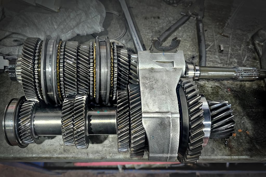 Manual transmission gear assembly and shafts on a workbench for automotive repair.