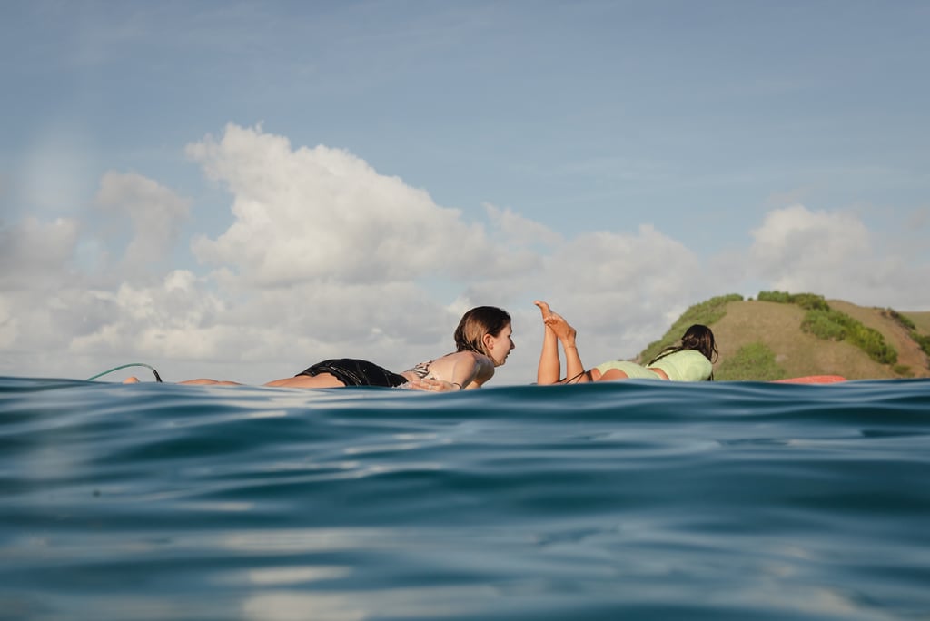 Two women lying on surfboards paddling out to the lineup in the ocean.