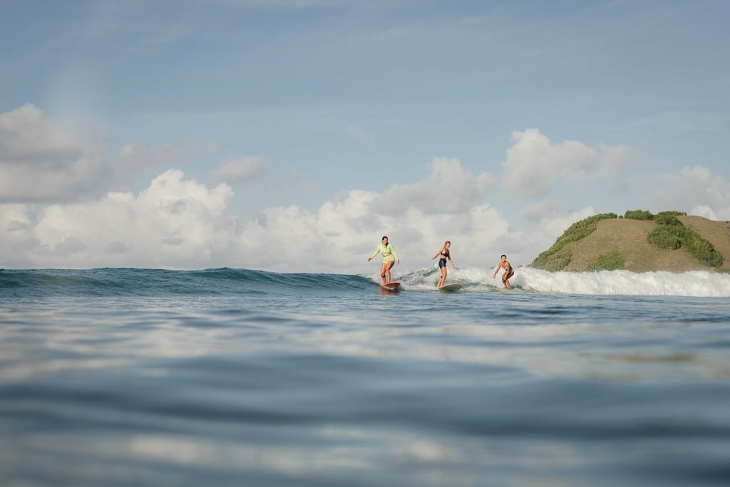 Three surf students riding the same wave on longboards, smiling and having fun.