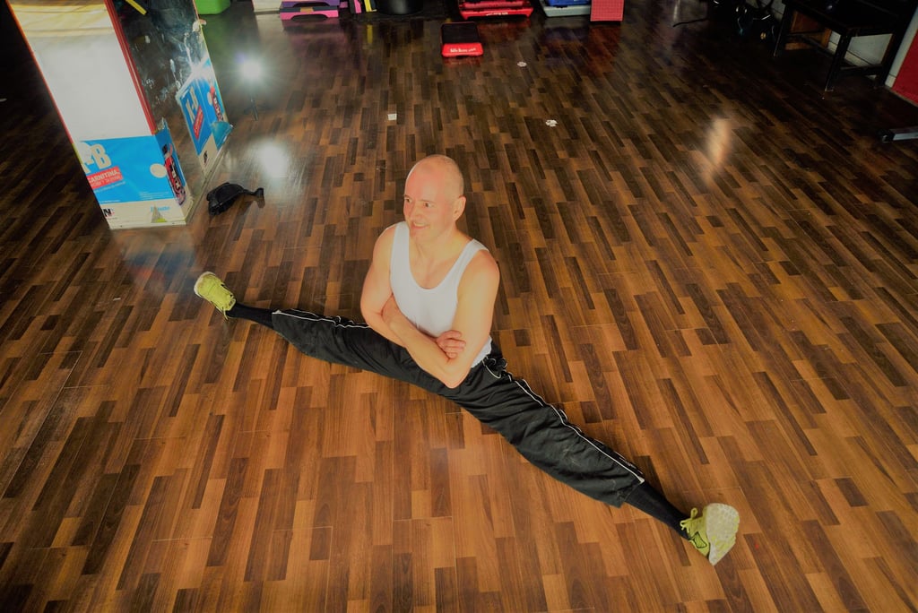 Jörg Grube im Fitnessraum auf dem Boden im Spagatsitz