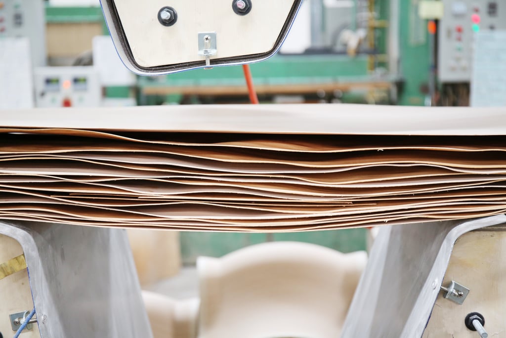 Stacked thin wood veneer sheets being processed in a furniture manufacturing plant.