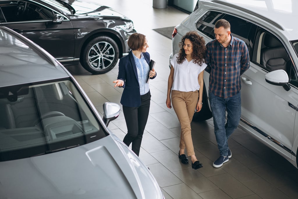  A female car saleswoman talks to a couple, walking through a car showroom.