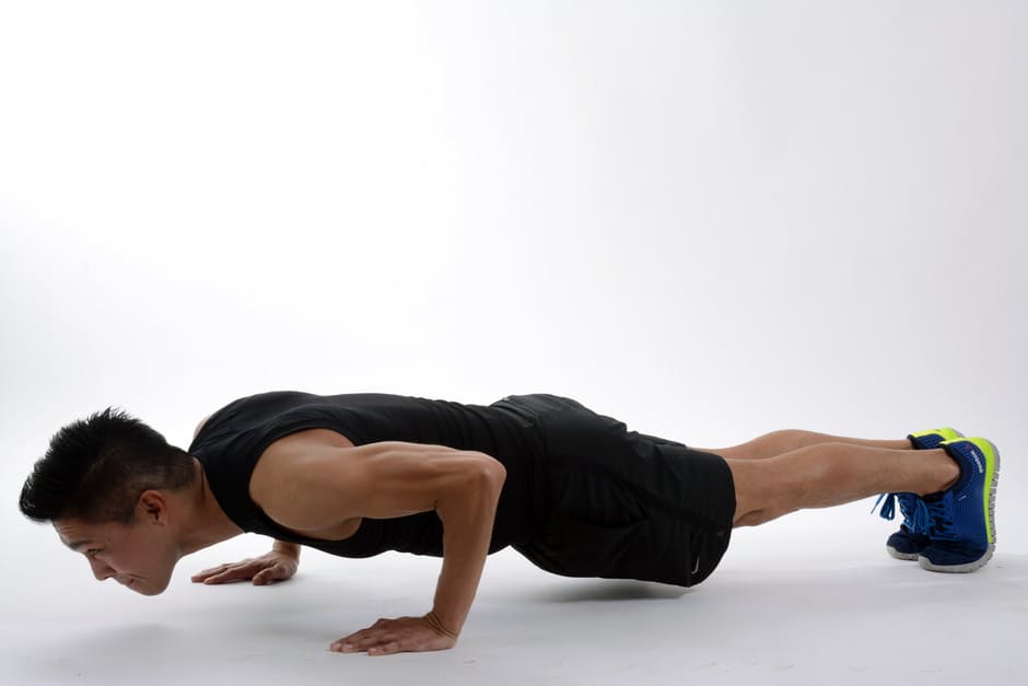 A person with lean arm muscles is in plank position in a white room.