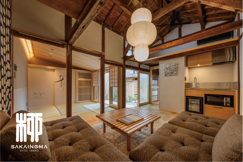築200年の町家を改装した一棟貸切宿「SAKAINOMA HOTEL 柳」の客室内部。高い梁を見せた天井と畳の和室、中庭に面した縁側、檜風呂につながる落ち着いた空間が広がり、ソファやキッチンも備えられている様子｜堺市のニュースならサカイタイムズ