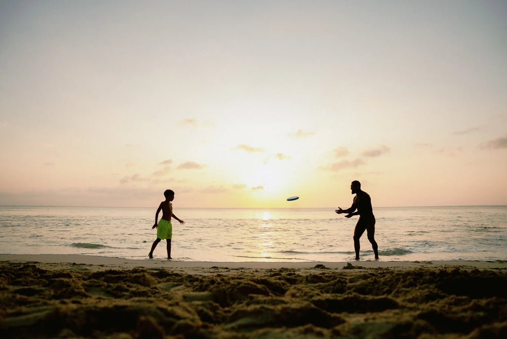 Family enjoying a frisbee game at sunset during a candid beach photography session at Dreamland Beach Bali.