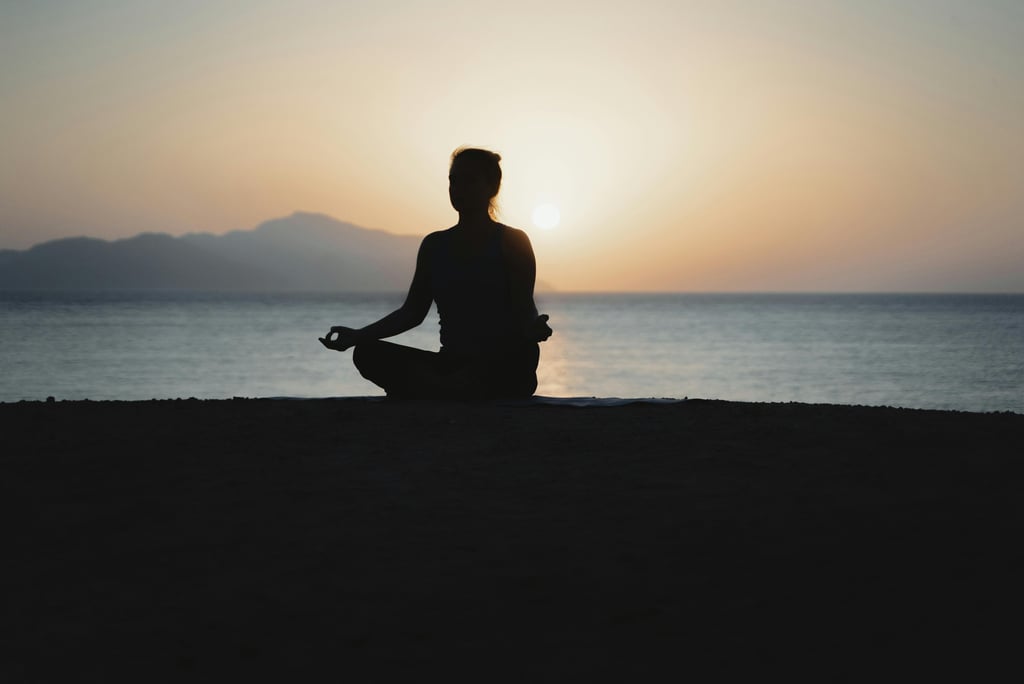 a meditating person sitting on a beach with a sunset in the background