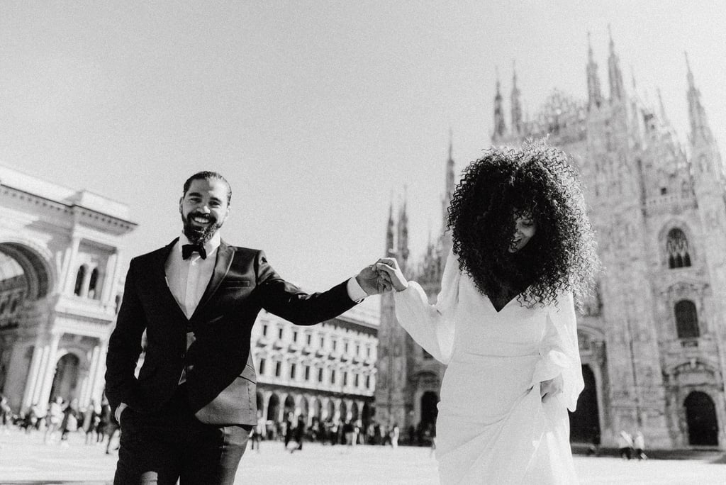 a man and woman holding hands and walking through in Milan Piazza Duomo