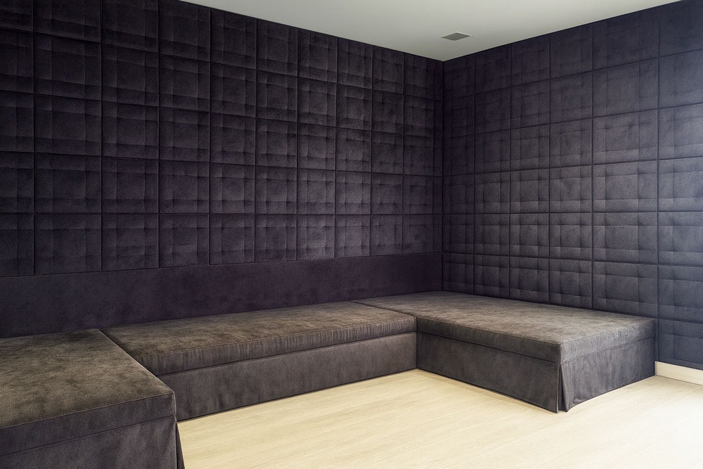 Modern corner design with custom upholstered wall panels and matching L-shaped seating in dark fabric by Solo Home Decor.