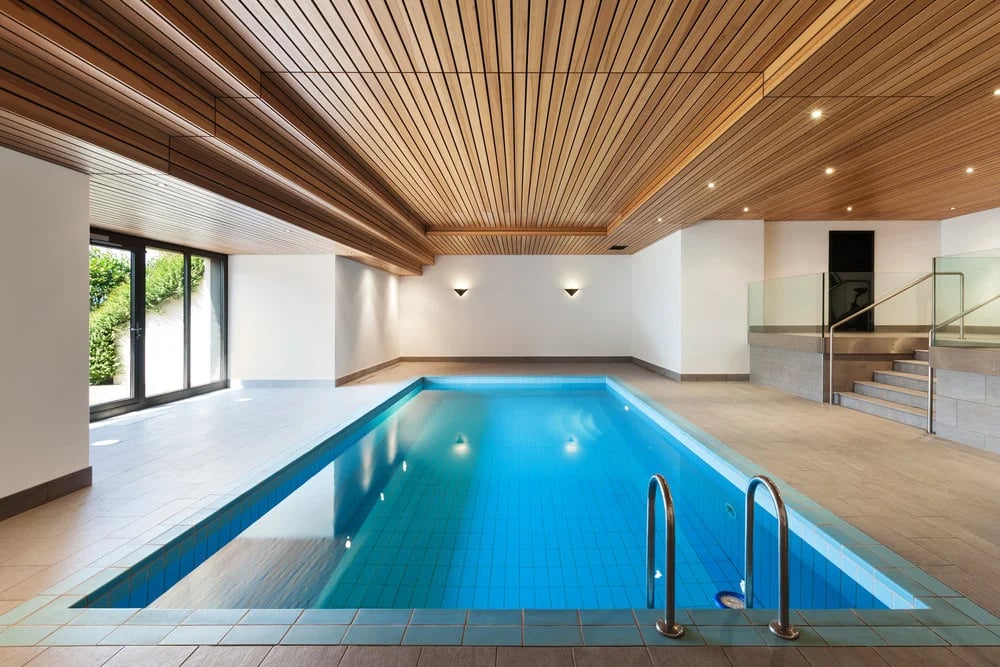 Modern luxury indoor swimming pool featuring a natural wood slat ceiling and bright blue tiling.