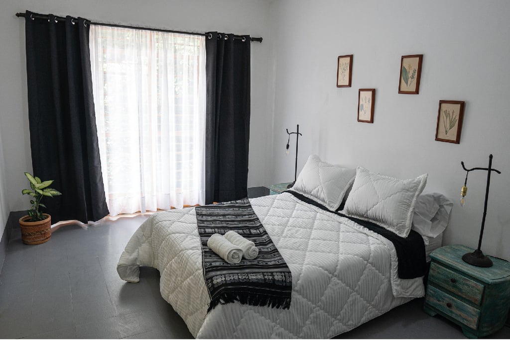 Modern guest bedroom with a white quilted bed, black curtains, and rustic wooden nightstands.