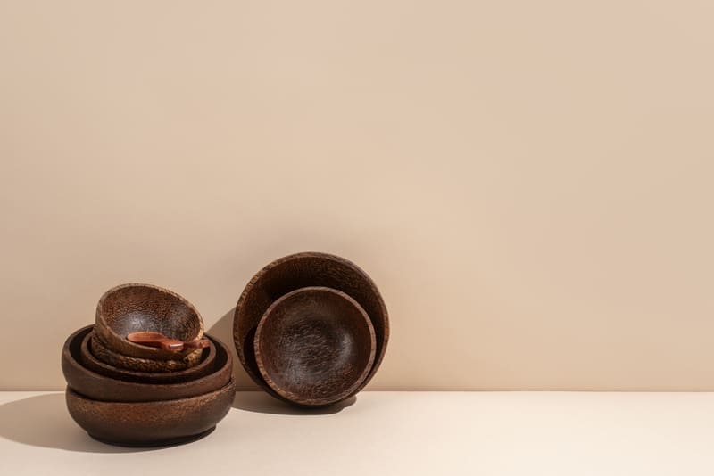 Cuencos artesanales de madera oscura y una pequeña cuchara de madera apilados sobre un fondo beige 