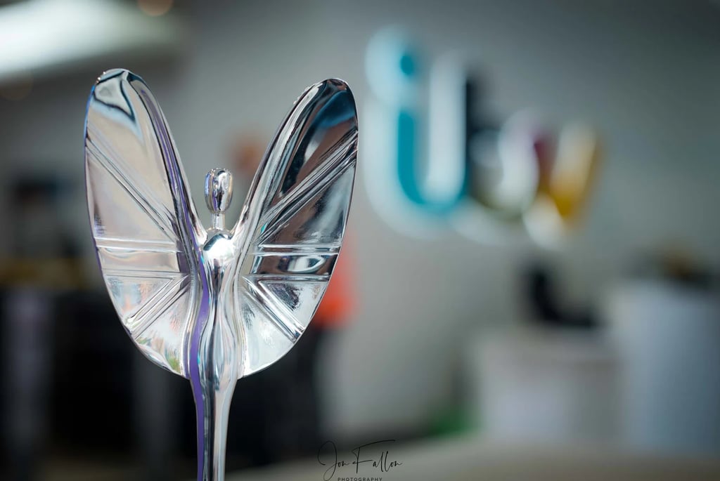 Polished silver trophy figurine with wings in front of a blurred ITV logo background.