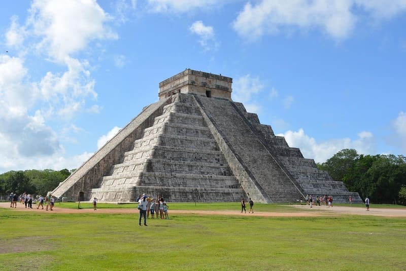 Die antike Maya-Pyramide El Castillo in Chichén Itzá unter blauem Himmel mit Touristen im Vordergrun