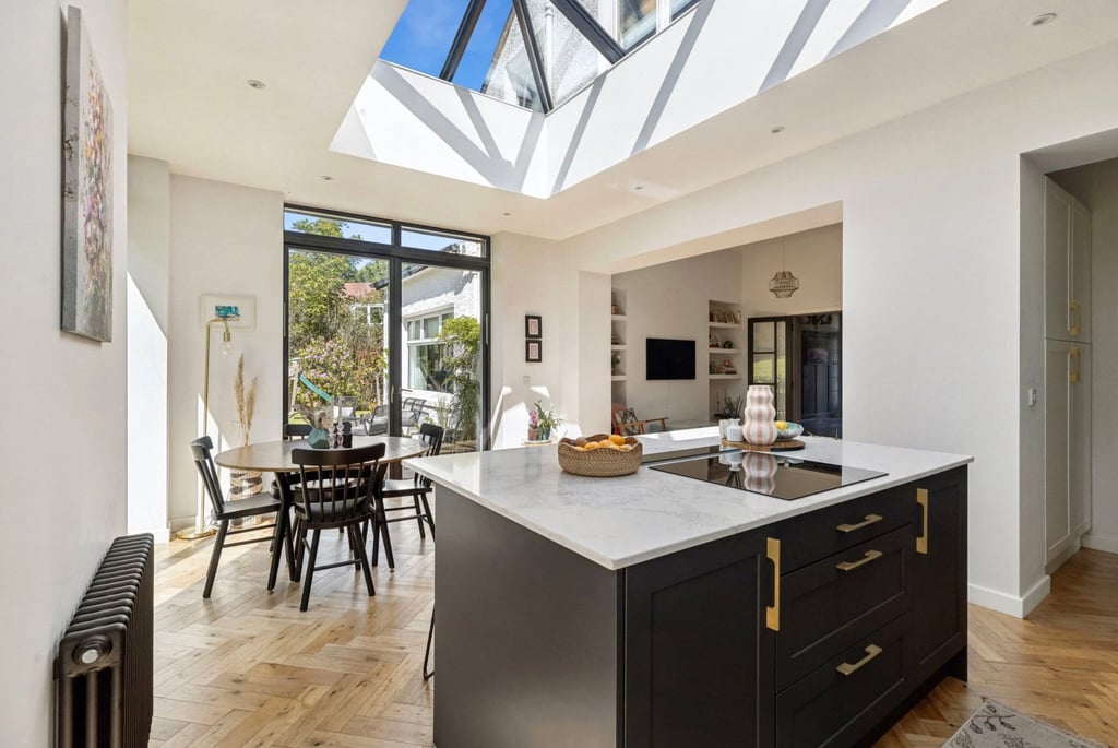 Modern open plan kitchen featuring a dark island with marble countertop and a large skylight roof lantern.