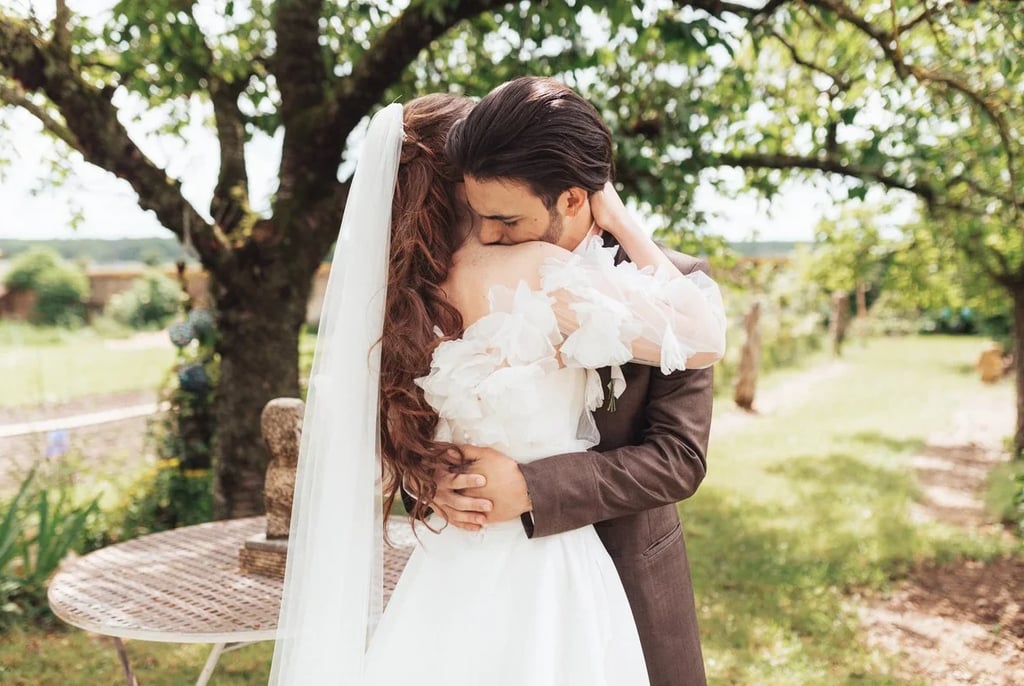 Mariés s’enlaçant lors de leur découverte dans un jardin arboré.