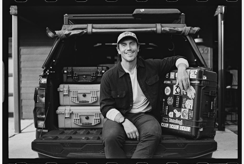 A smiling photographer sitting on a truck tailgate with outdoor gear and Pelican cases.