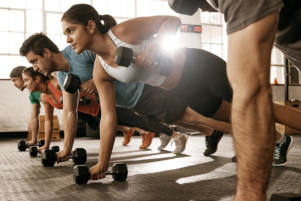 Diverse group performing renegade rows with dumbbells during a high-intensity gym workout.