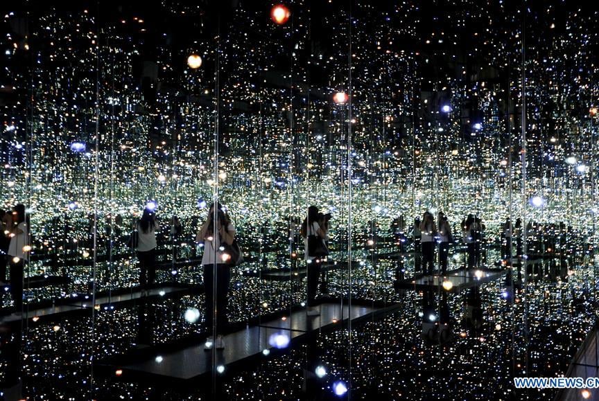Sala espelhada com luzes suspensas que parecem infinitas, criando a ilusão de um universo de estrela