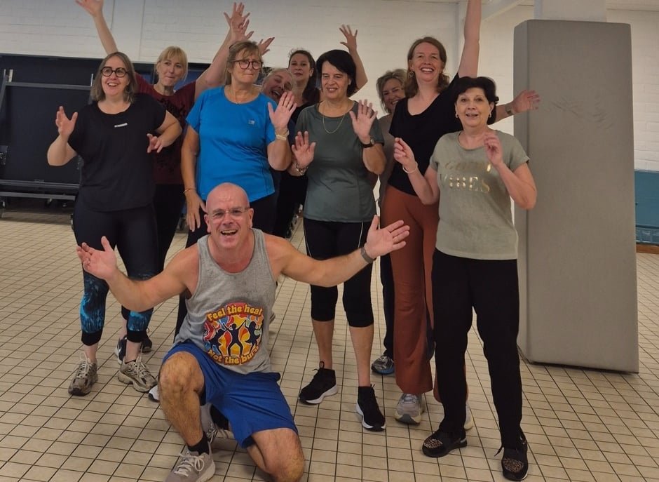 Group of smiling adults after a Groove Fitness disco class in Leuven, with Richard kneeling at the front, arms open