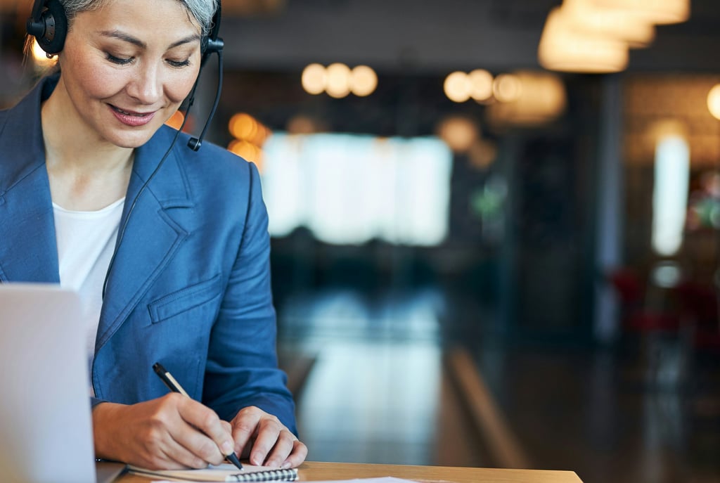 Businesswoman in headphones making notes while sitting at a desk with a laptop