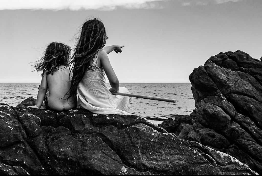 two girls sitting on rocks with a stick in their hands