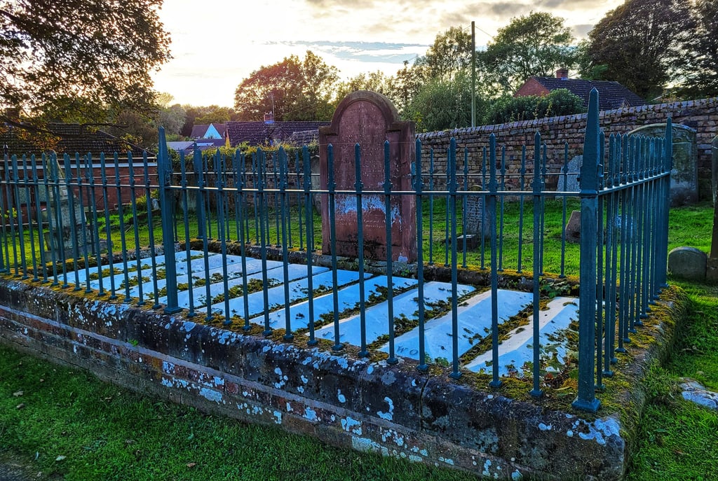 A historic stone grave of The Nine men enclosed by a green iron fence in an old cemetery at sunset.