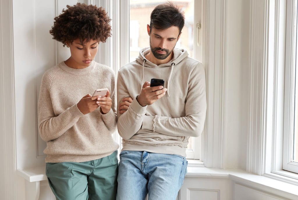 a man and woman standing next to each other and texting
