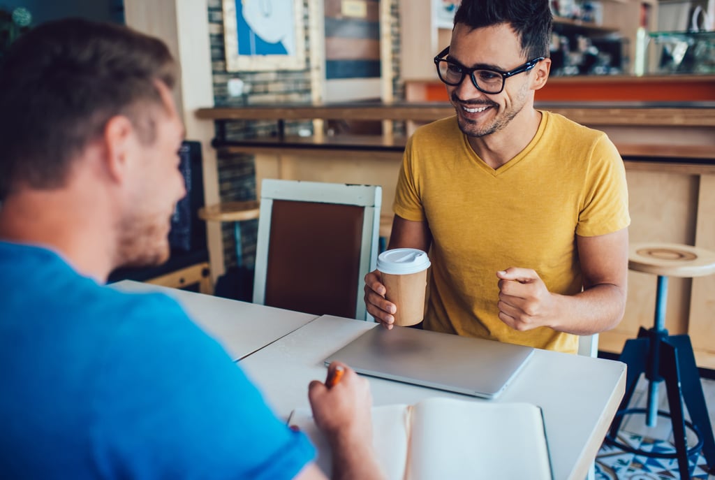 Two professionals having a coffee meeting, with one taking notes during an informational interview.