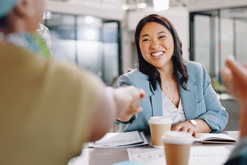Professional smiling and shaking hands across a table during a meeting, suggesting a successful job 