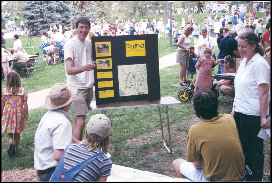 A man holding a trifold with "PedNet" information on it speaking in front of a small crowd