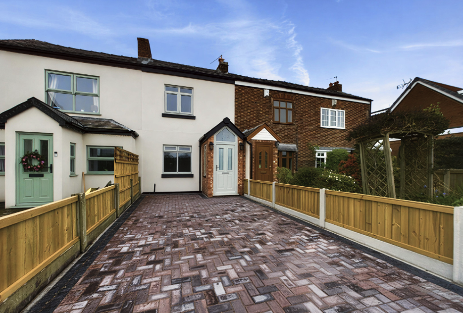 A modern block paved driveway and wooden panel fencing in front of a white semi-detached house.