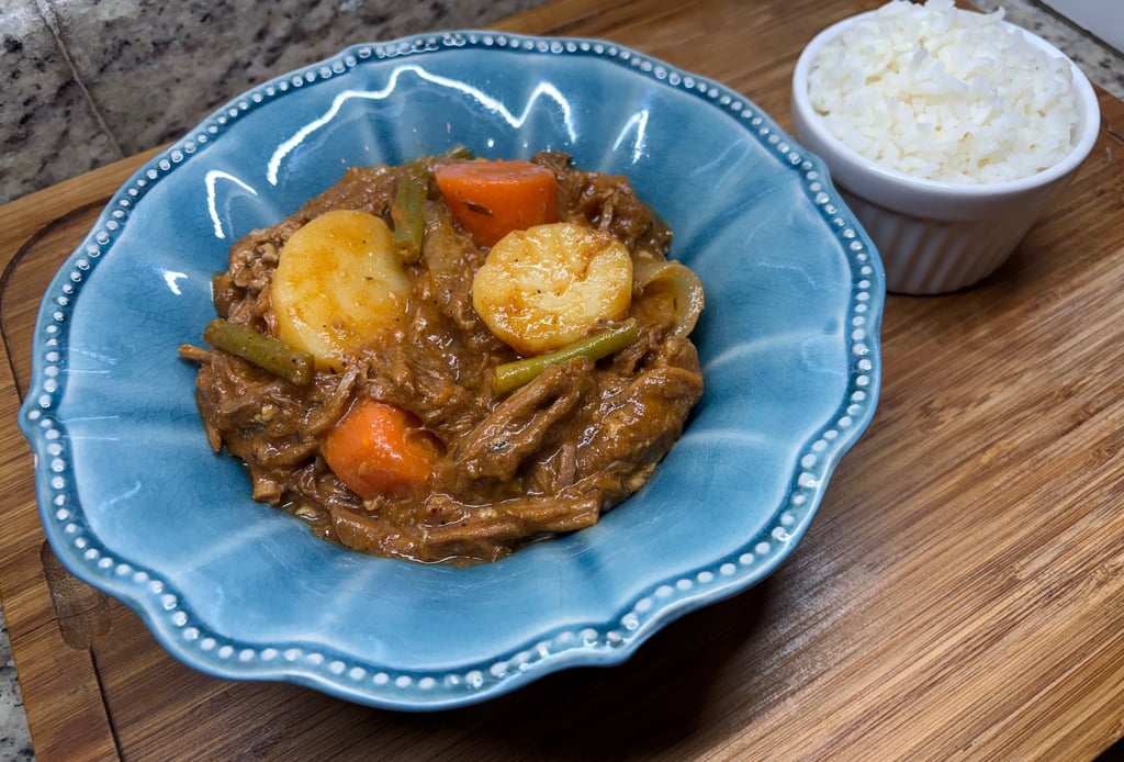 Slow-cooked beef stew with potatoes and carrots in a blue bowl served with a side of white rice.