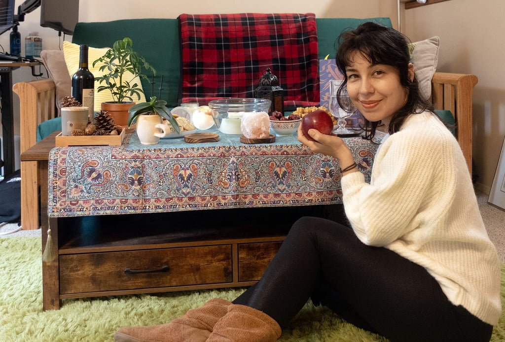 Woman sitting on the floor holding a red apple beside a decorated table