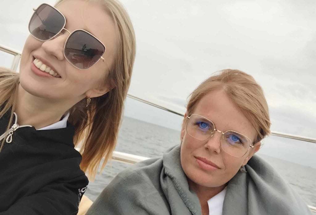 Dwie kobiety na katamaranie. Jedna w okularach przeciwsłonecznych i czarnej bluzie.